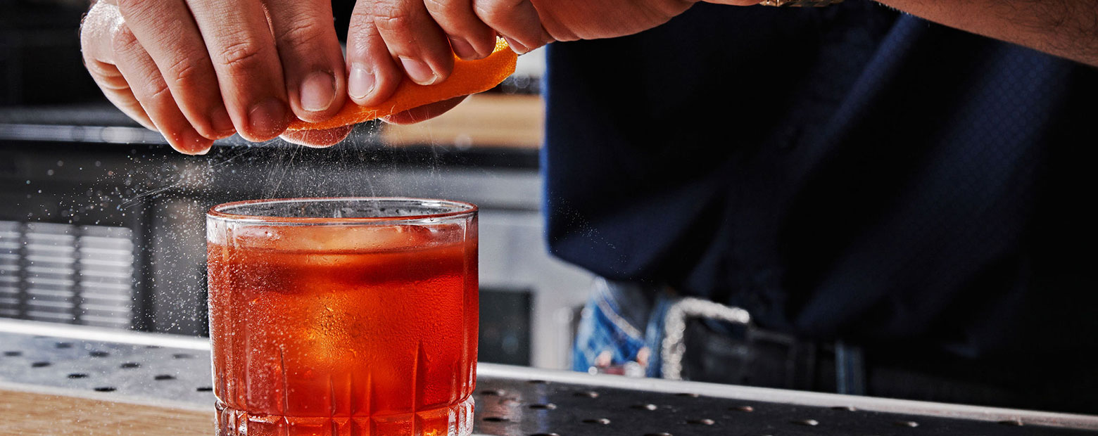 bartender squeezing orange slice into cocktail
